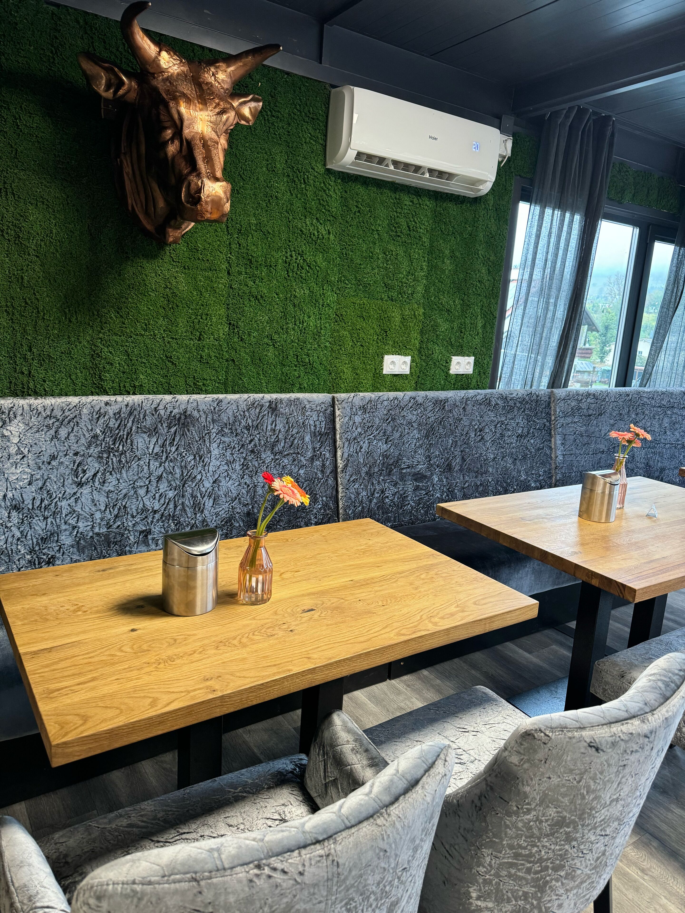 A restaurant interior with a green wall, a mounted cow head decoration, and a modern air conditioning unit.