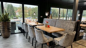 Un restaurant moderne avec des tables en bois et des chaises à revêtement gris, de grandes fenêtres offrant une vue sur l’extérieur.