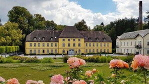 Un grand bâtiment jaune à la façade symétrique, entouré de jardins bien entretenus et sous un ciel dégagé.