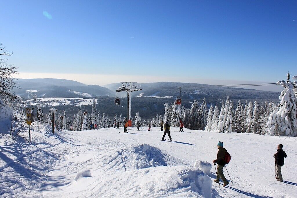 A snowy ski slope with skiers, a ski lift, and a clear view of the surrounding mountains.