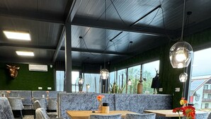 Un restaurant moderne avec des tables hautes et des banquettes confortables, agrémenté d’un mur végétal et de grandes fenêtres.