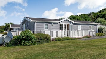 Une maison mobile à deux étages, avec une clôture en bois peinte en blanc, une antenne parabolique et une pelouse bien entretenue.