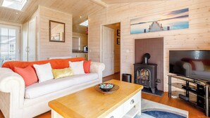 A cozy living room with a wooden ceiling, a white sofa with colorful cushions, a wooden coffee table, a fireplace, and a television.