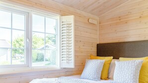 A bedroom with a large window, wooden walls, a bed with white and yellow bedding, and a headboard.