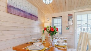A dining area with a wooden table set for four, a vase with red flowers, and a painting on the wall.