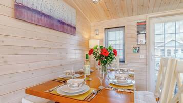 Un coin repas avec une table en bois dressée pour quatre personnes, un vase rempli de fleurs rouges et un tableau accroché au mur.