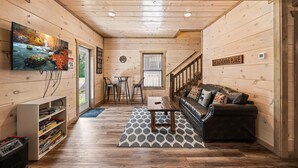 A cozy cabin interior with wooden walls, a sofa, a coffee table, and a TV on the left wall. - NEW Cabin 10mins to Dollywood★HotTub★BBQ★GSMNP★PetsOK★Highspeed WiFi★PvtBackyard (Pigeon Forge)