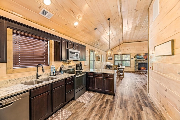 A cabin-style kitchen with wooden walls, dark cabinets, granite countertops, and a stone fireplace.