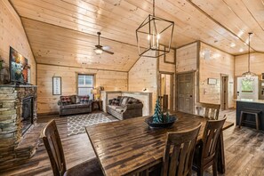 A spacious log cabin interior with a dining area, two sofas, a fireplace, and a stone wall.
