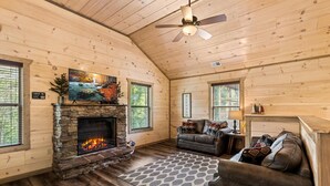 A cozy cabin interior with a stone fireplace, a leather sofa, and a ceiling fan. - NEW Cabin 10mins to Dollywood★HotTub★BBQ★GSMNP★PetsOK★Highspeed WiFi★PvtBackyard (Pigeon Forge)