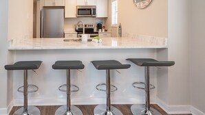 A modern kitchen with a marble countertop, stainless steel appliances, and three bar stools.