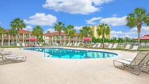 A pool area with lounge chairs, palm trees, and a building with a red roof.