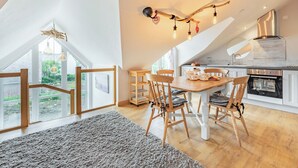 Moderni keittiö, jossa on valkoiset kaapit, puinen ruokapöytä ja näkymä vehreään maisemaan.