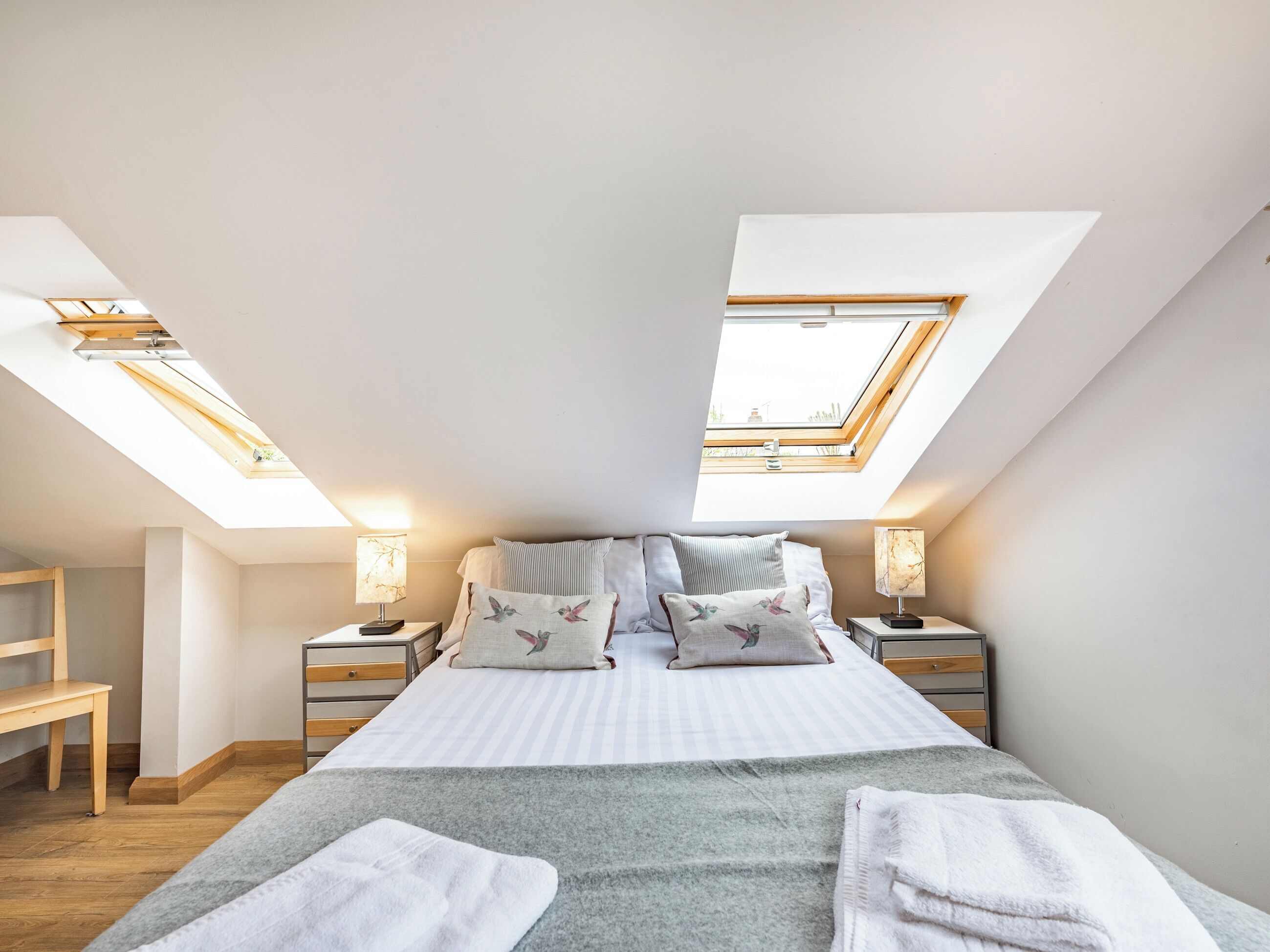 A bedroom with a skylight, a bed with pillows, bedside tables, and a bench.
