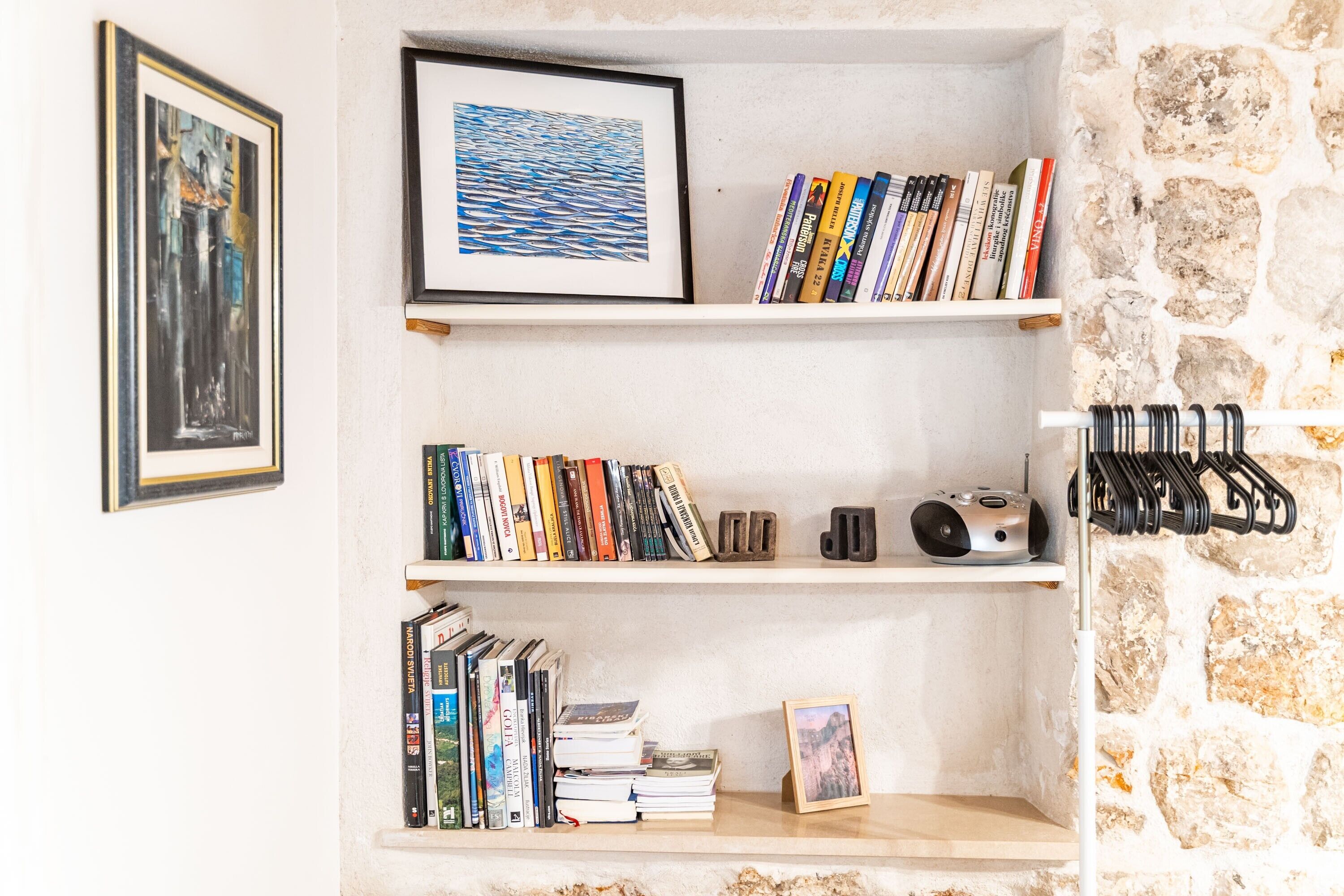 A bookshelf with books and framed pictures against a stone wall.