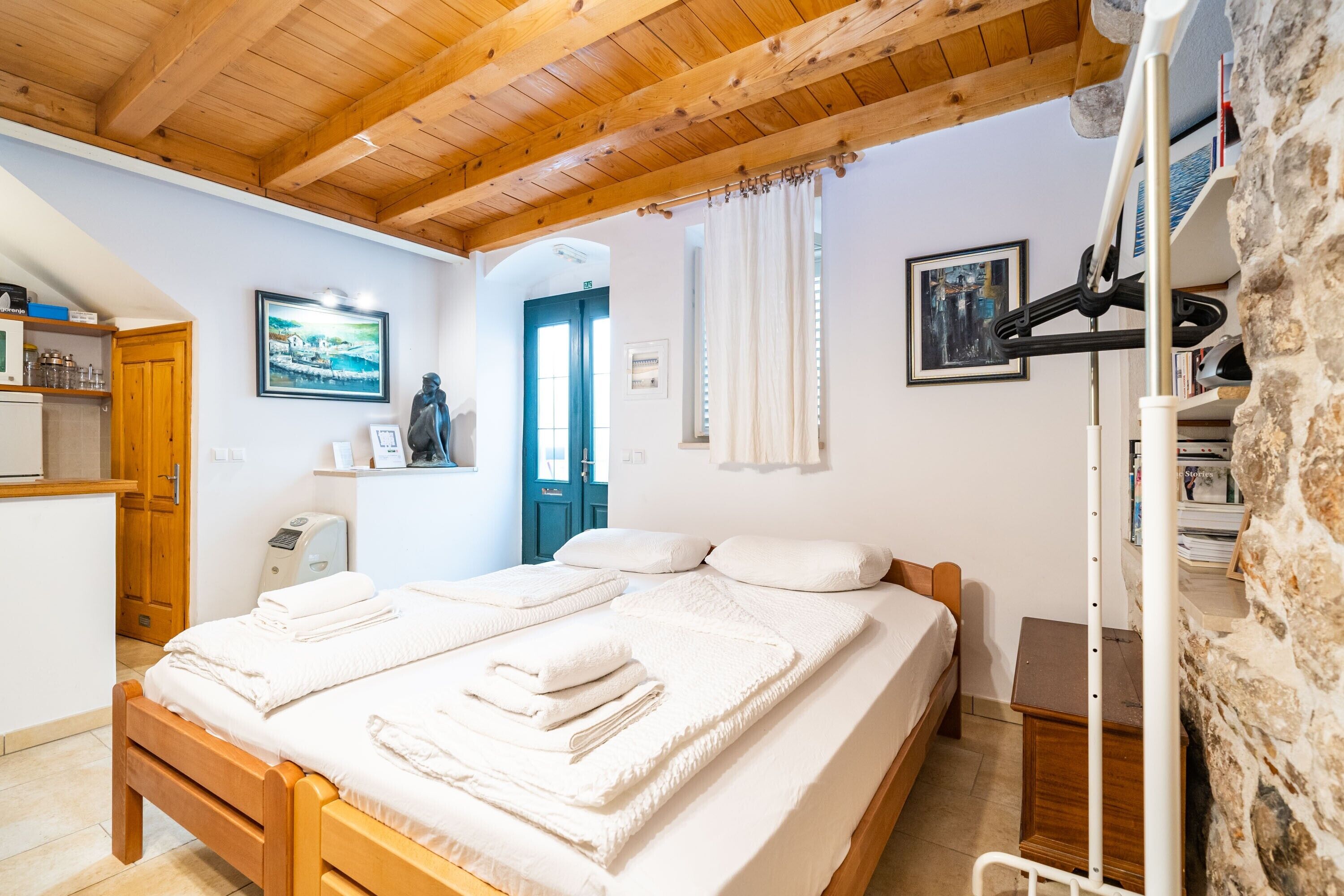 Ein Zimmer mit einem Holzbett, weißer Bettwäsche, einer Steinwand und einer Holzbalkendecke.