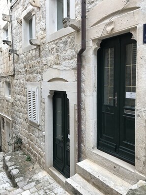 A narrow street with stone buildings, a black door, and a window with shutters. - Apartments Ribambit- One Bedroom Apartment (First Floor) (Dubrovnik)