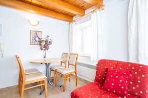 A room with a wooden ceiling, a red sofa, a dining table with chairs, and a window with curtains. - Apartments Ribambit- One Bedroom Apartment (First Floor) (Dubrovnik)