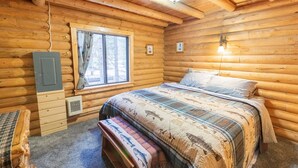 A log cabin room with a bed, bench, window, wall-mounted light, and electrical box.