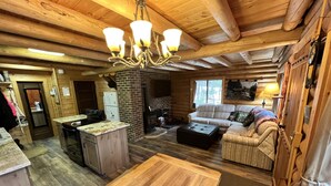 A cozy cabin interior with a wooden dining table, a sofa, and a fireplace.