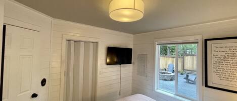 Un dormitorio con cama, televisor montado, ventana con vista al exterior y lámpara en el techo.