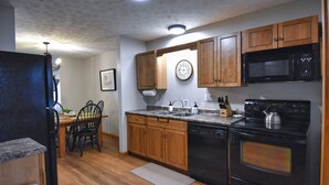 Una cocina con armarios de madera, un microondas negro, una estufa y un comedor con mesa y sillas.