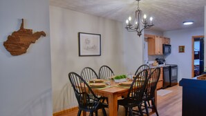 Un comedor con una mesa de madera dispuesta para seis comensales, sillas negras, una araña y un dibujo enmarcado en la pared.