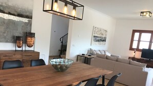 Una sala de estar moderna con una mesa de comedor de madera, sillas negras, un sofá beige y un tazón de vidrio grande sobre la mesa.