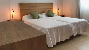 Una cama doble con cabecera de madera, dos almohadas verdes y una colcha blanca. Hay dos mesitas de noche con lámparas.