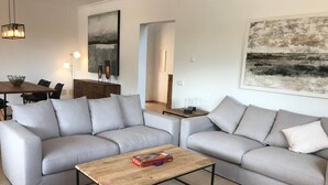 Una sala de estar moderna con dos sofás grises, una mesa de centro de madera y una zona de comedor al fondo.