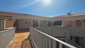 A courtyard with a tiled floor, a white railing, and a building with a tiled roof and a chimney.