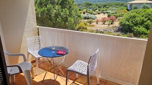 A balcony with a table and chairs, a view of greenery and mountains, and a tiled floor.