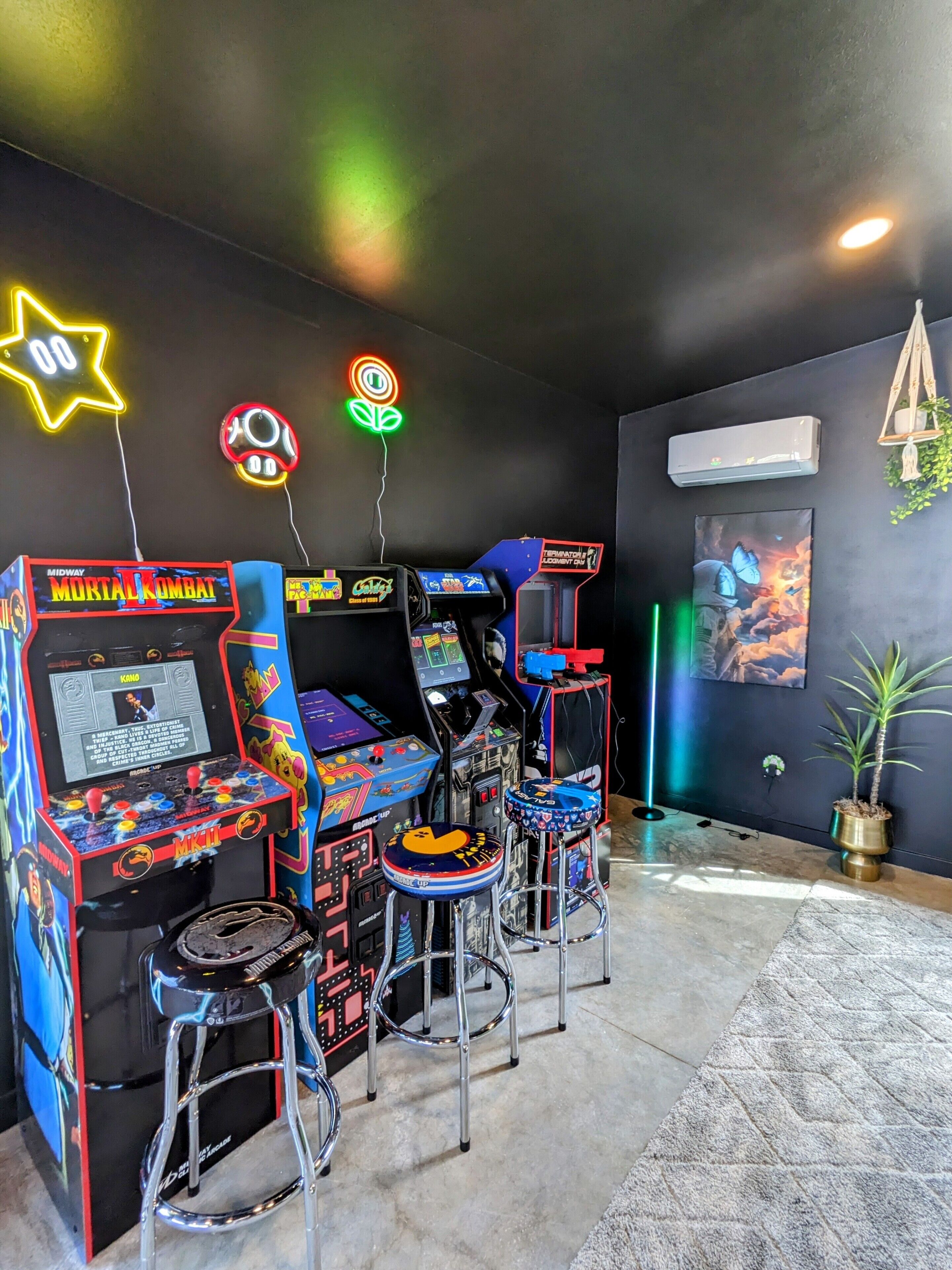 Une salle d’arcade à l’ambiance rétro, avec des néons, des bornes d’arcade classiques et des tabourets en métal.