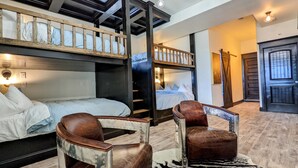 Une chambre d’hôtel avec des lits superposés, une échelle en bois, un fauteuil en cuir et un tapis à motifs zébrés.
