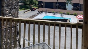 Vista da un balcone con un muro in pietra, una piscina e un lago sullo sfondo.