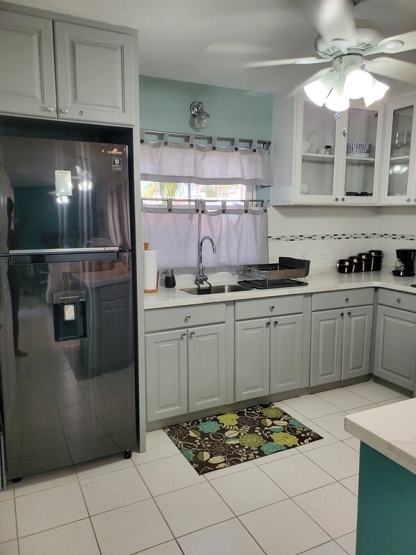 A kitchen with white cabinets, a stainless steel refrigerator, a sink, and a ceiling fan. - 2 mins to beach! Family sized condo with a pool. Super close to dining and fun! (Dover)