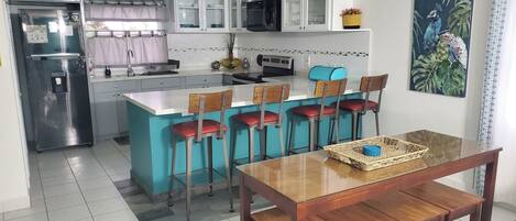 A kitchen with a central island, bar stools, a dining table, and a refrigerator.