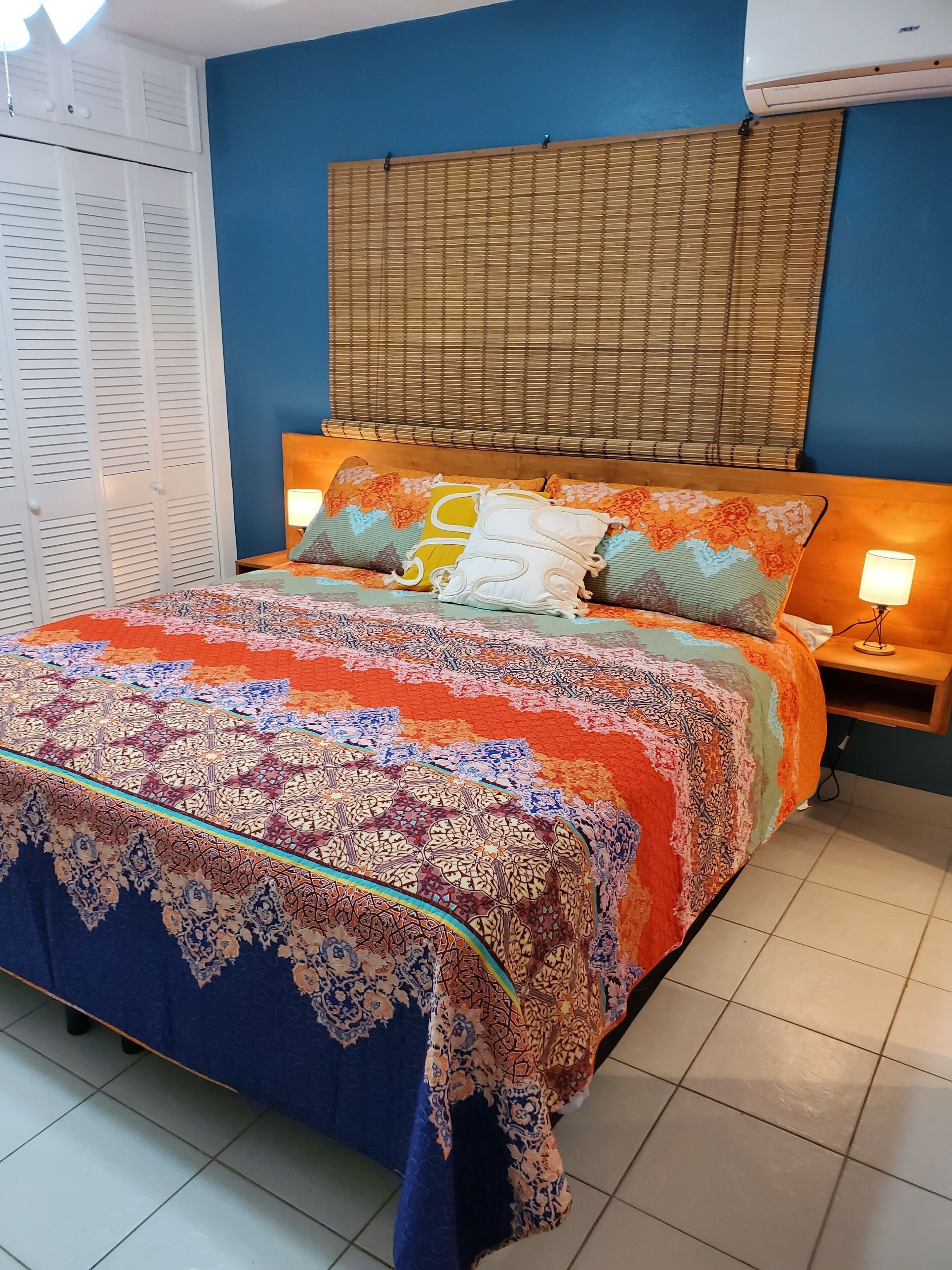 Een slaapkamer met een bedovertrek met patroon, een houten hoofdbord en een nachtkastje met een lamp.