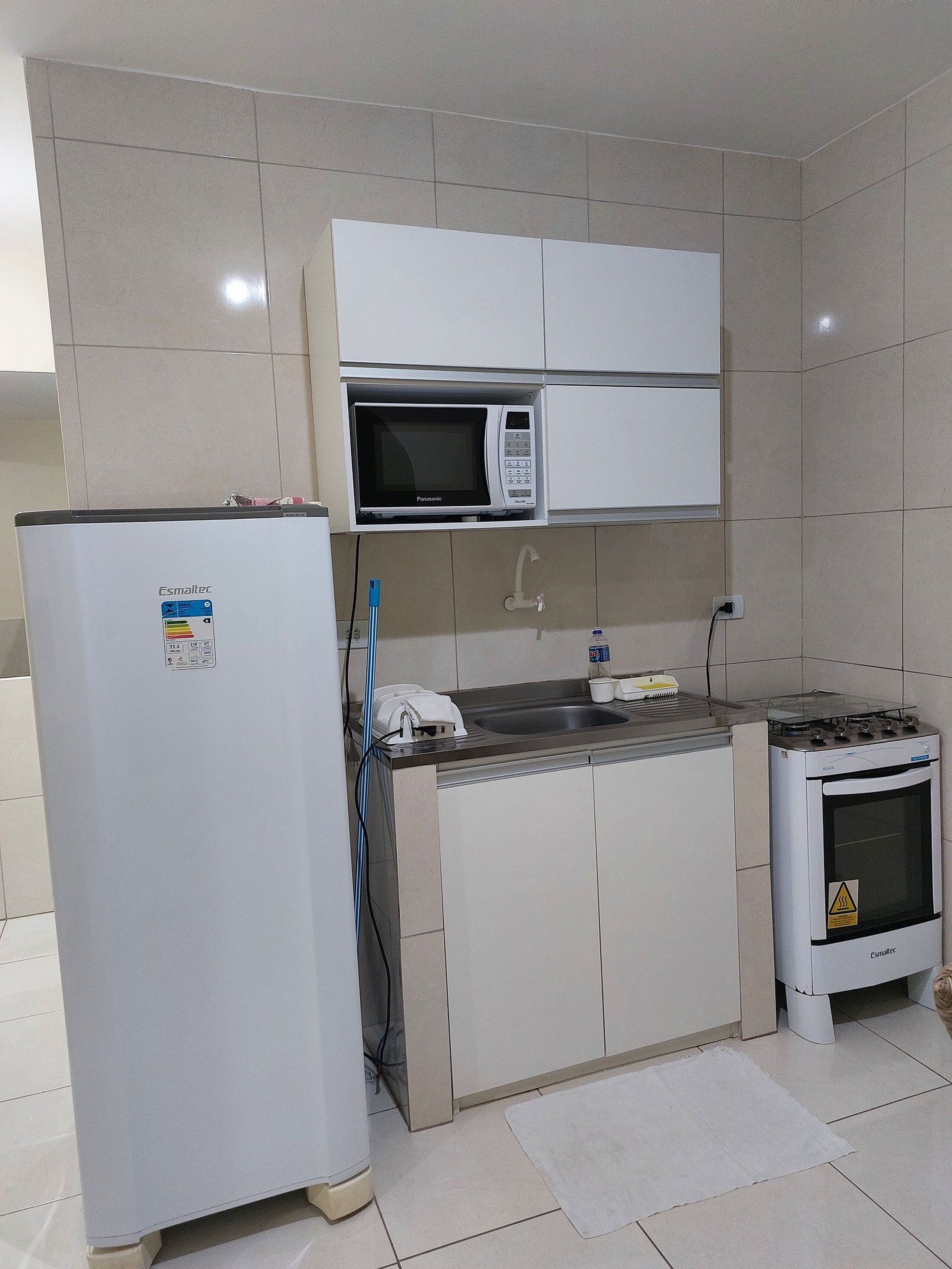 A compact kitchen with a refrigerator, microwave, sink, and stove.