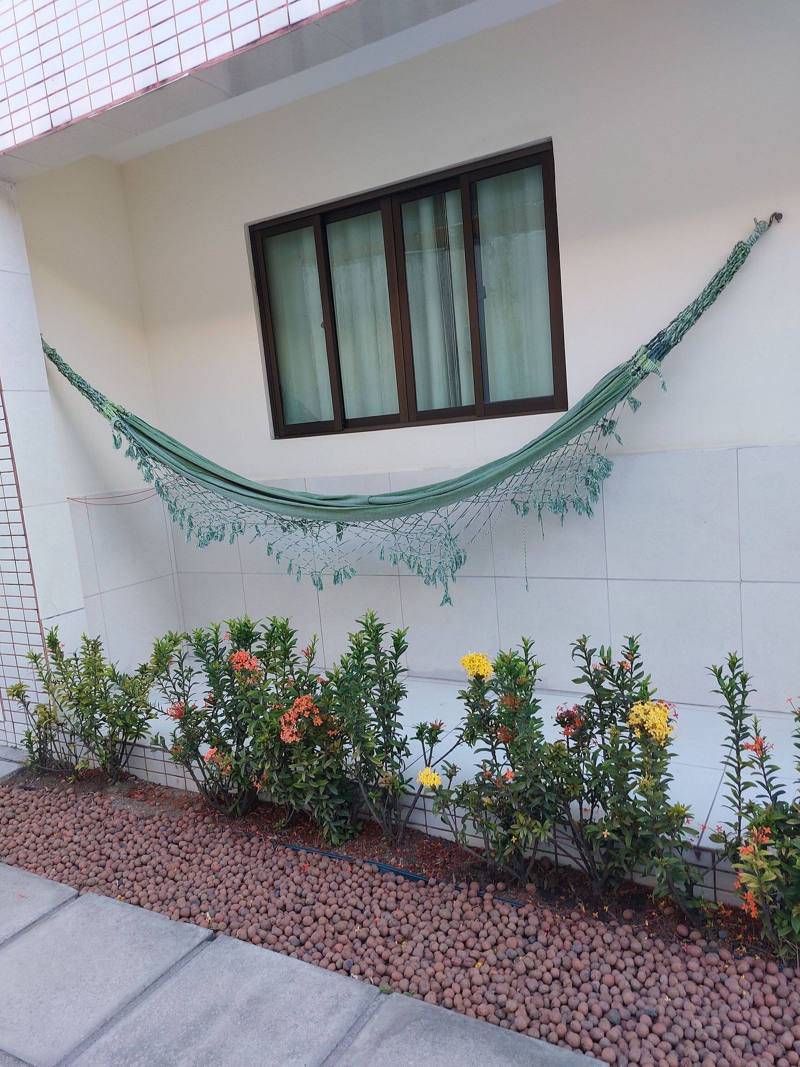 A building exterior with a hammock, window, and flower beds.