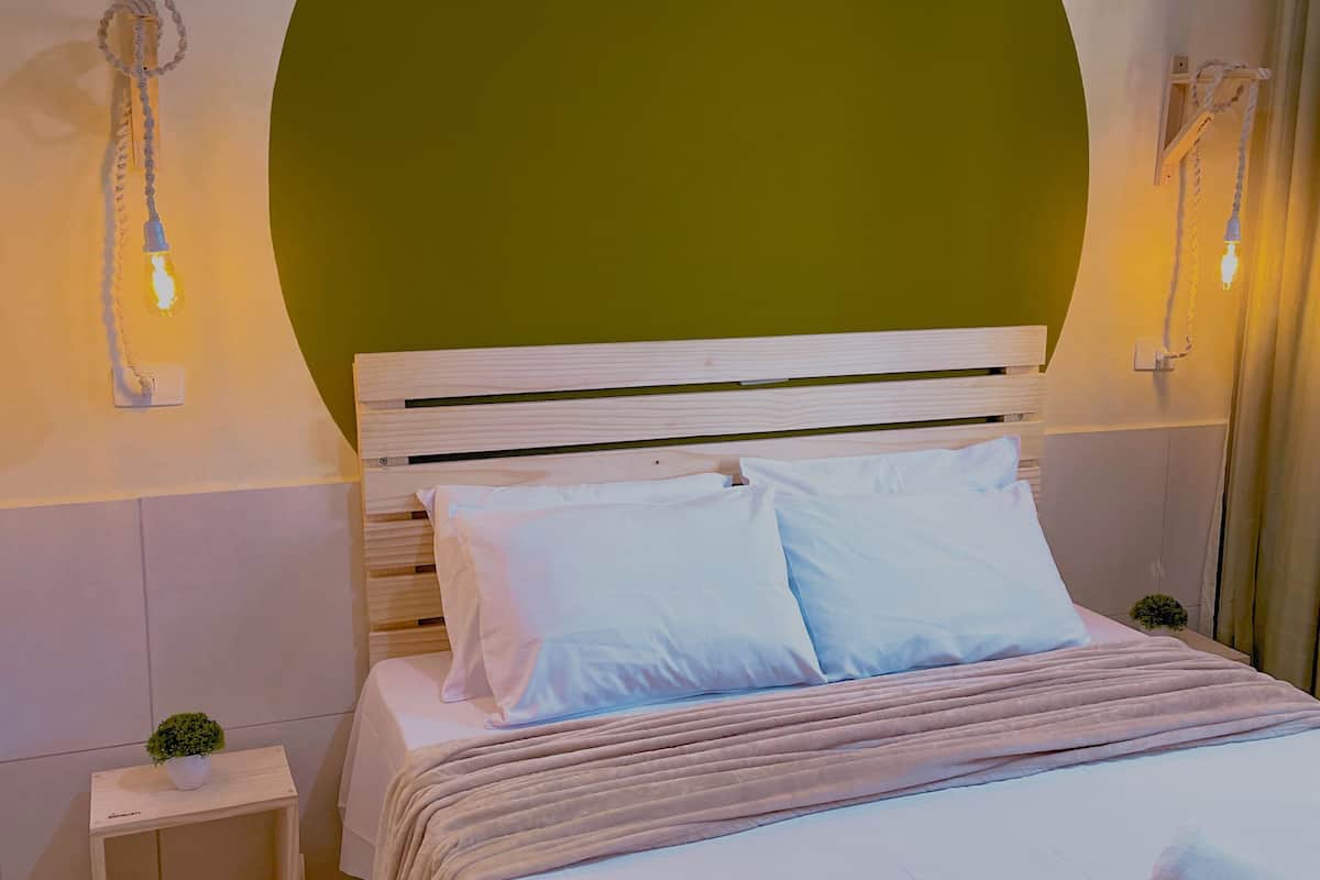 A bedroom with a large bed, a nightstand, a wall-mounted lamp, and a green accent wall.