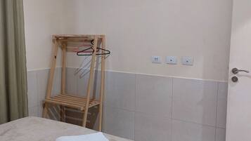 A hotel room with a bed, an air conditioning unit, a wooden chair, and a towel on the bed.