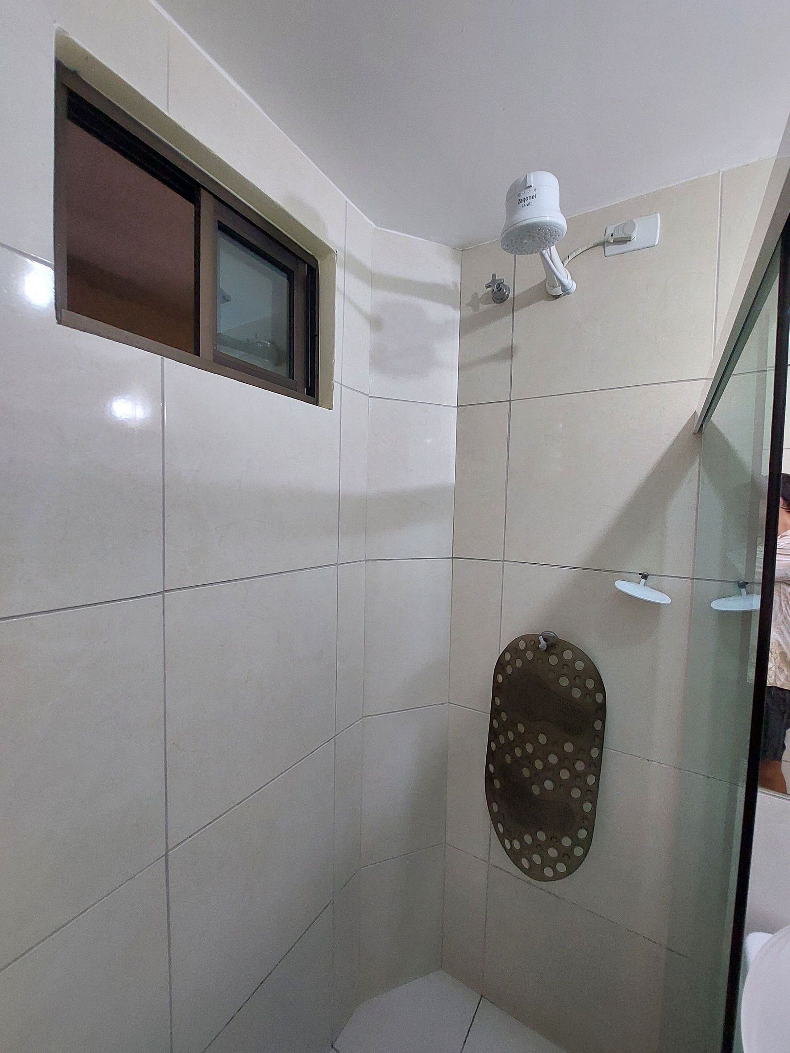 A small, tiled bathroom with a shower, a toilet, and a window.