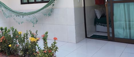 A building with a tiled exterior, a window with a curtain, a door with a glass panel, and a small garden area with pebbles and plants.