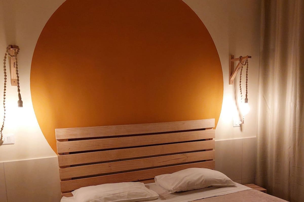 A hotel room with a large bed, wooden headboard, two bedside lamps, a nightstand, and a curtain.