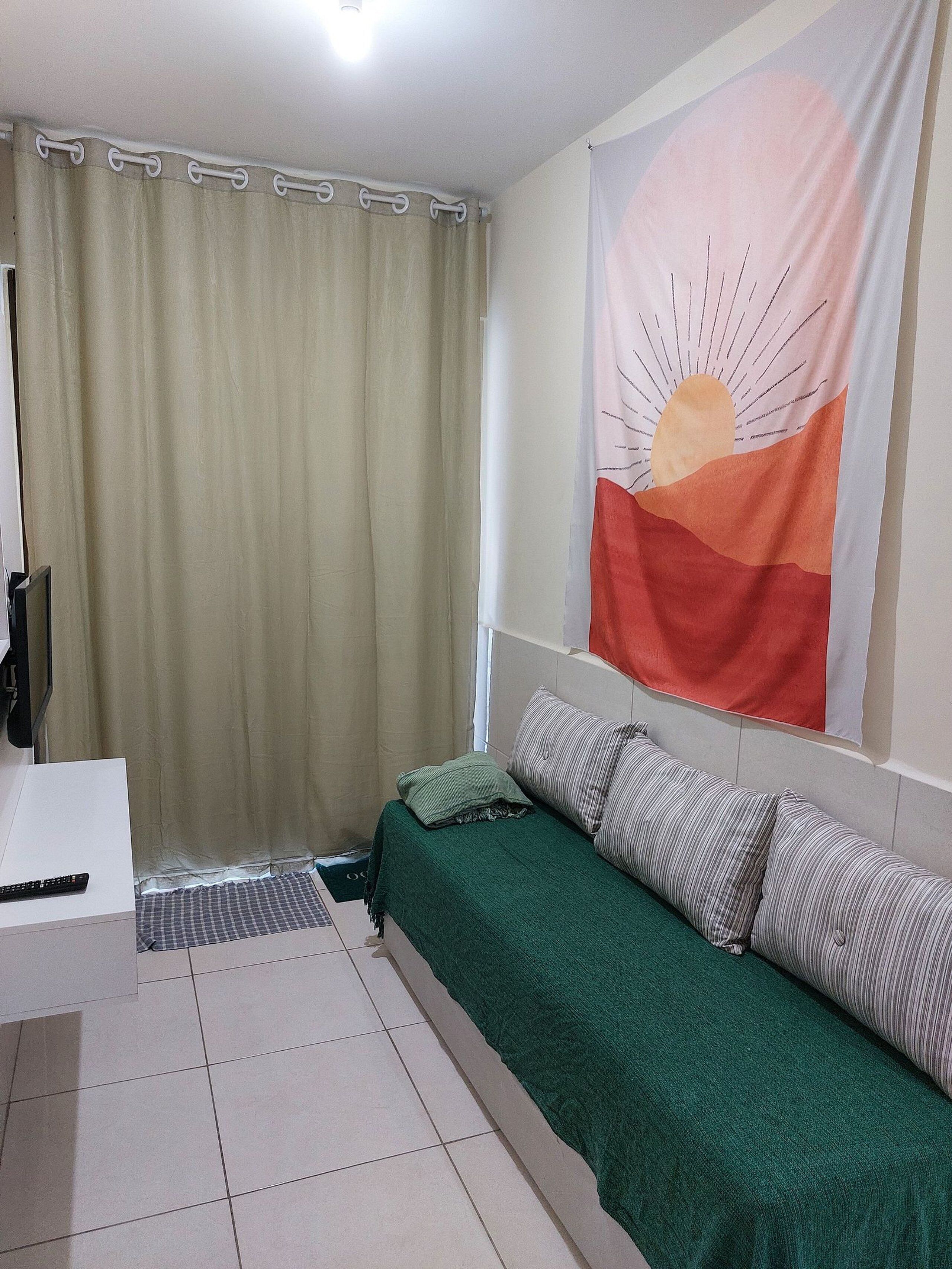 A small, tidy room with a bed, a desk, and a curtain.