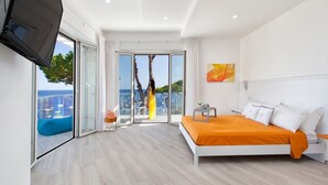 Un dormitorio moderno con una cama grande, televisor y balcón con vistas al mar.