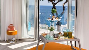 Una habitación con vista al mar, una mesa con alimentos para el desayuno y un bolso sobre un taburete.