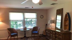A room with two wicker chairs, a small round table, a wooden dresser, and a large mirror.