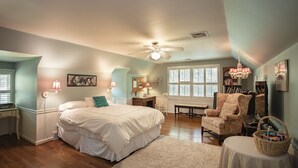 A bedroom with a large bed, a chair, a desk, and a window.